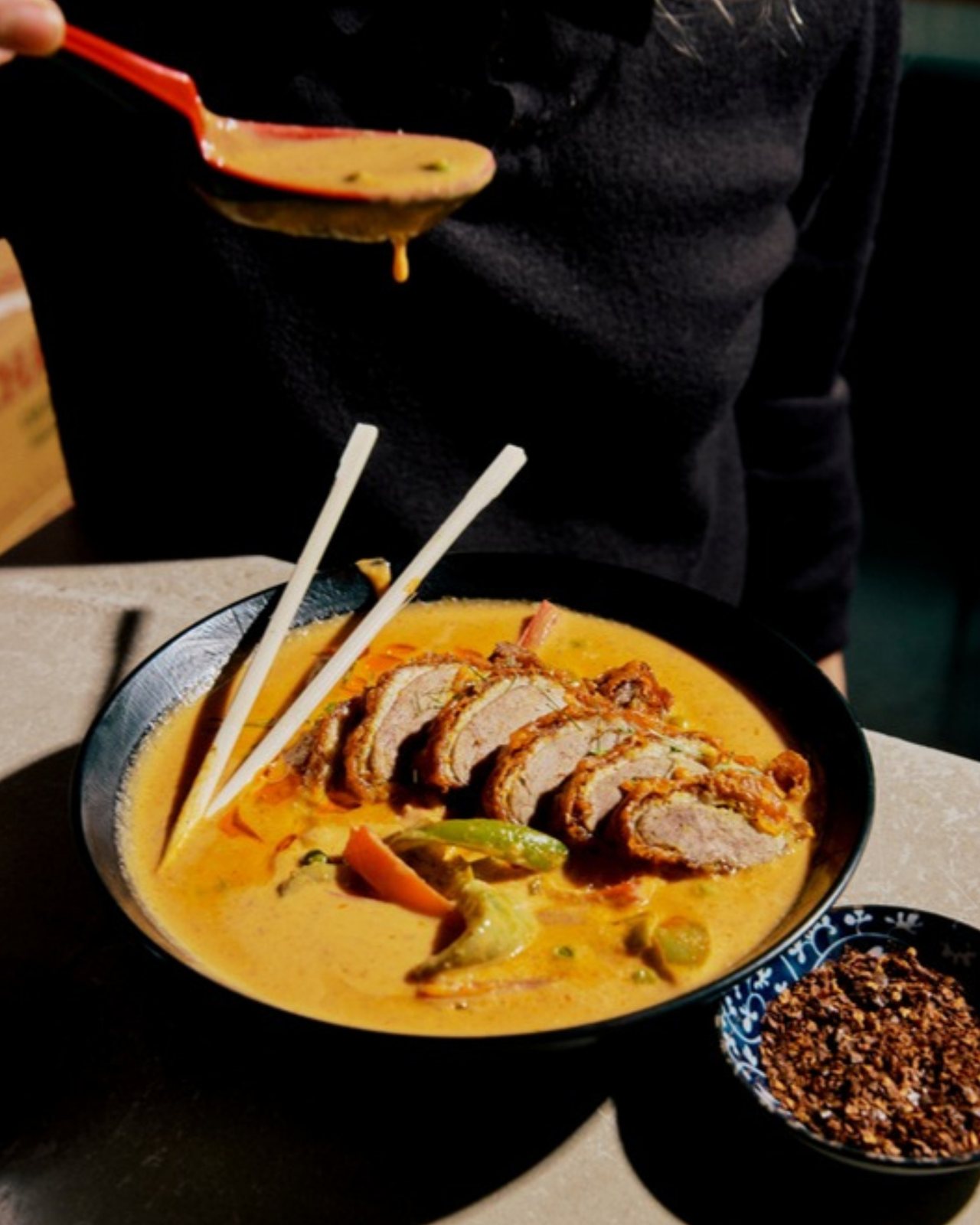 Zoo Thai duck red curry: sliced crispy duck in a coconut curry bowl with chopsticks, a red ladle pouring more curry above it